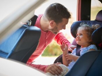 padre che mette in auto la figlia su seggiolino