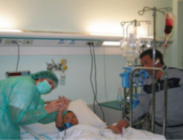 camera di ospedale con un bambino sul lettino, un infermiere e un uomo